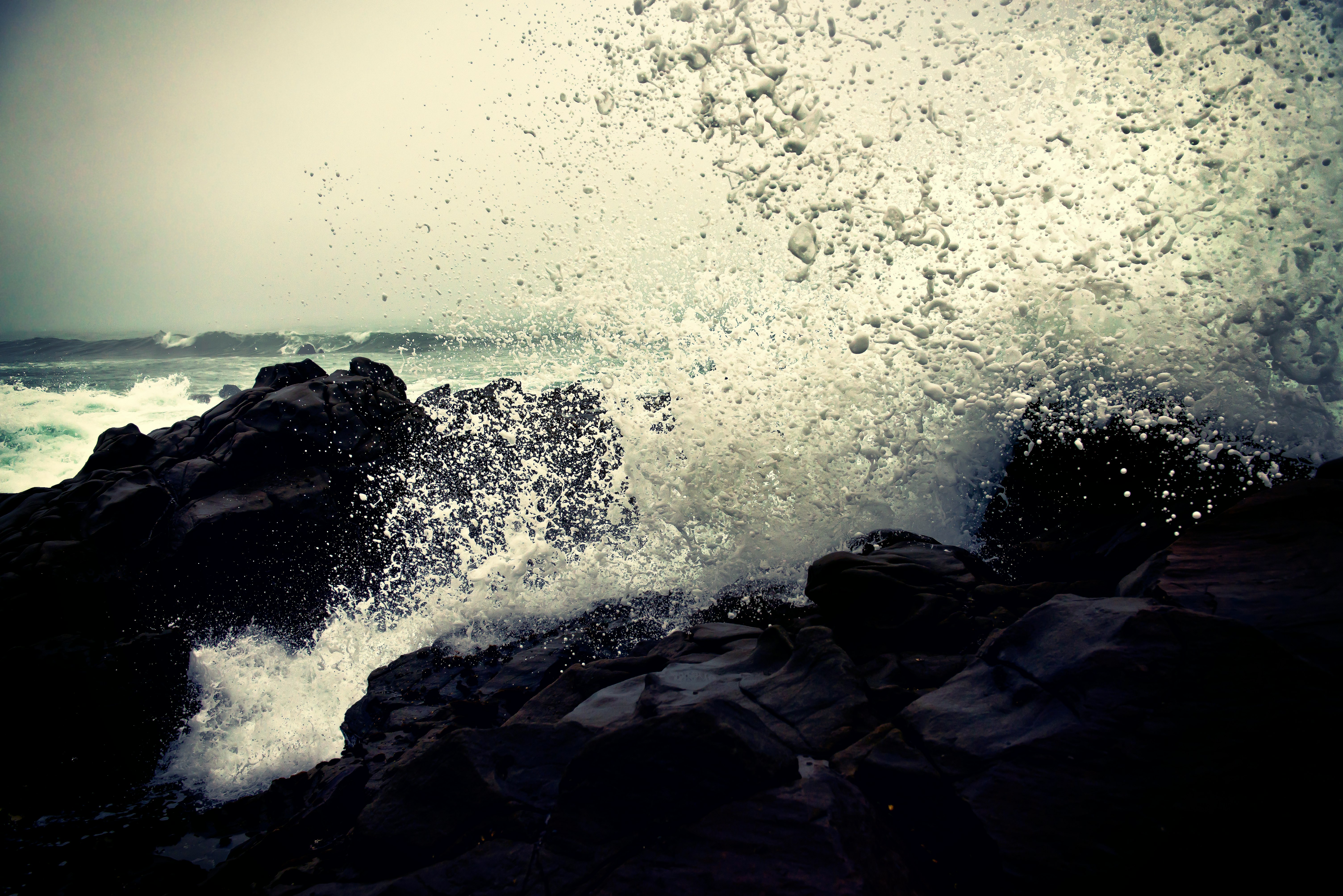 grayscale photography of ocean waves crashing on rock during daytime